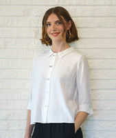 model in a black pant with a white button down blouse with 3/4 sleeves, a split cuff, and a twin button detailing