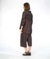 model in a pullover top with a dropped shoulder, rounded hem and oversized cowl neckline. worn with a matching pant with a double overlap at the top of each leg. top and pant are striped in varying shades of reds and browns