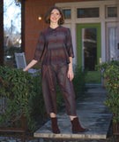 model in a boxy button down blouse with a 3/4 sleeve and twinbutton detail. fabric is striped with varying shades of reds, blues and oranges. worn with a matching pant with an overlap at both legs