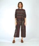 model in a boxy button down blouse with a 3/4 sleeve and twinbutton detail. fabric is striped with varying shades of reds, blues and oranges. worn with a matching pant with an overlap at both legs