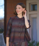 model in a boxy button down blouse with a 3/4 sleeve and twinbutton detail. fabric is striped with varying shades of reds, blues and oranges. worn with a matching pant with an overlap at both legs