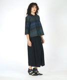 model in a boxy button down blouse with a 3/4 sleeve and twinbutton detail. fabric is striped with varying shades of blues. worn with a wide leg black pant