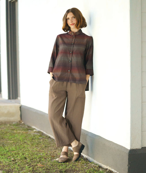 model in a button down blouse with a 3/4 sleeve with a split cuff, a double collar and a striped print in varying shades of reds and browns. worn with a wide leg brown pant