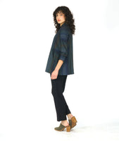 model in a button down blouse with long sleeves, a standing collar, and contrasting directional panels on the body. fabric is striped with varying shades of blues. worn with a slim leg black pant