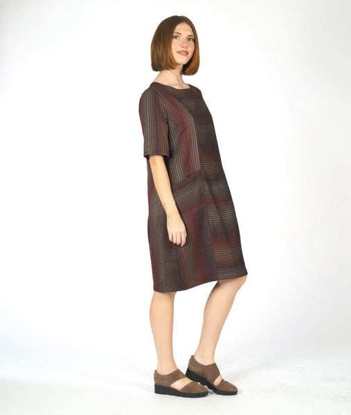 model in a striped dress with short sleeves and contrasting panels at the body at the princess seams and pockets. dress is striped with varying shades of red and brown