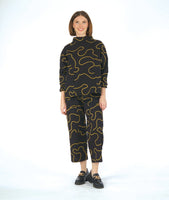 model in a wide leg black pant with cargo pockets, worn with a matching pullover blouse with a standing cowl neckline, dropped shoulders, princess seams and a full boxy body. pants and top are black with a yellow swirl print embroidered all over