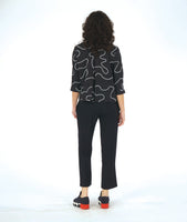 model in a slim black pant with a black button down blouse with 3/4 sleeves and a twin button detail. blouse has a white swirl print embroidered all over