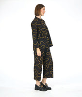 model in a wide leg pant with low pockets, worn with a matching blouse with long sleeves and a standing mandarin style collar. pants and blouse are both black with a yellow swirl pattern embroidered all over