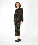 model in a wide leg pant with low pockets, worn with a matching blouse with long sleeves and a standing mandarin style collar. pants and blouse are both black with a yellow swirl pattern embroidered all over