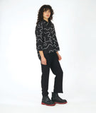 model in a slim black pant with a black button down blouse. blouse has a high low hem and a white swirl print embroidered all over