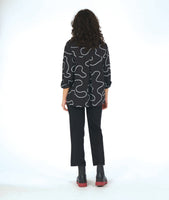 model in a slim black pant with a black button down blouse. blouse has a high low hem and a white swirl print embroidered all over