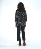 model in a slim black pant with a black button down blouse. blouse has a high low hem and a white swirl print embroidered all over