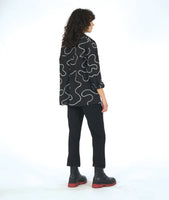model in a slim black pant with a black button down blouse. blouse has a high low hem and a white swirl print embroidered all over