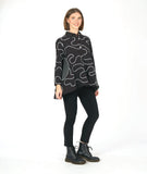 model in a black legging with a black button down blouse. blouse has 3/4 sleeves, a solid black collar, and a full bell shaped silhouette. blouse is black with a white swirl pattern embroidered all over, with round patches in a black and white grid print