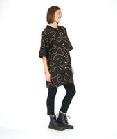 model in a black leggin with a black cocoon shape shirt dress with a yellow swirl print embroidered all over. dress has solid black cuffs and collar