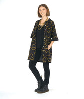 model in a black leggin with a black cocoon shape shirt dress with a yellow swirl print embroidered all over. dress has solid black cuffs and collar. dress is worn open over a solid black top with layers of gold necklaces