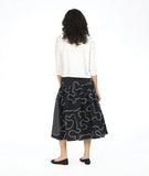 model in a white boxy button down blouse with a black skirt. skirt is gathered at the hip and is black with a white swirl print embroidered all over, and large circular patches with a black and white grid print