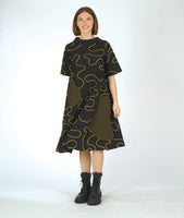 model in a bell shaped dress with pockets, 3/4 raglan sleeves, and a standing round collar. dress is black with a yellow swirl print embroidered all over, with round patches on black and yellow checker print