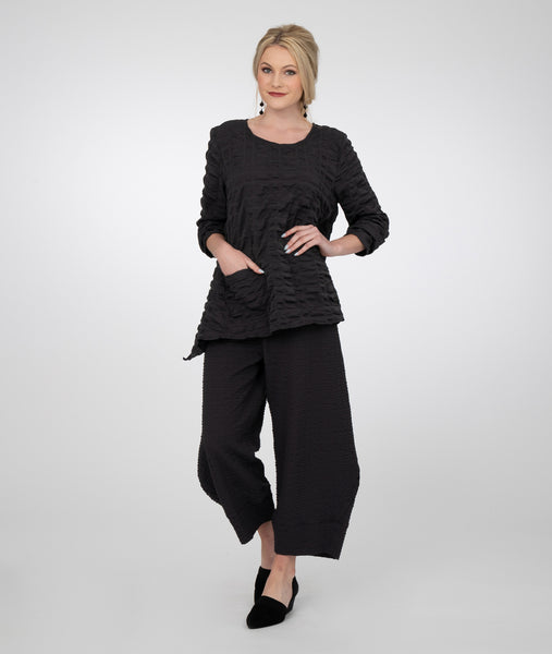 model in a textured, wide leg black pant that tapers down at the knee, with a larger texture matching top with a dropped hem at eiter side and a single hip pocket.
