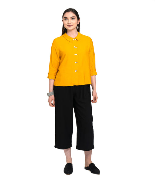 model in a wide leg cropped black pant with a boxy saffron yellow button down top with a twin button detail along the front, back and sleeve cuffs