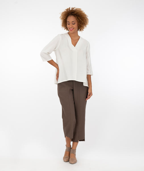 model in a white pullover blouse with 3/4 sleeves, a vneck, and a split at the front center seam. worn with a straight leg brown pant with a stair step hem