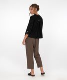 model in a slim brown pant with a boxy black button down top with a twin button detail along the front, back and sleeve cuffs