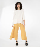 model in a white top with a hankerchief hem and hip pocket, worn with a buttery yellow pant with a drape detail on the sides