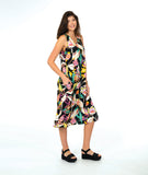 A woman modeling a sleeveless shift dress with a vibrant multicolor floral print on a black background, paired with black platform sandals, against a solid white studio background.