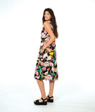 A woman modeling a sleeveless shift dress with a vibrant multicolor floral print on a black background, paired with black platform sandals, against a solid white studio background.