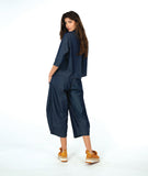 model wearing a dark wash chambray button down blouse with 3/4 sleeves and a twin button detail. worn with a matching barrel leg pant with oversized pockets and a yellow shoe