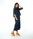 model wearing a dark wash chambray button down blouse with 3/4 sleeves and a twin button detail. worn with a matching barrel leg pant with oversized pockets and a yellow shoe