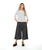 model in a wide leg black cropped pant with white dots, worn with a white pullover top with a cowl neck and black dots