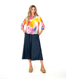 A woman modeling a colorful abstract print long-sleeve top with a cowl neck and 3/4 sleeves. paired with a dark chambray wide-leg pant 