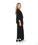 A woman modeling a black three-piece outfit consisting of a draped open-front jacket, wide-leg trousers, and a matching top, styled over a colorful floral print camisole and black block-heel sandals, against a plain white studio background.
