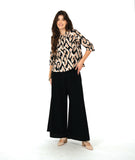A woman modeling a beige and black geometric patterned blouse with three-quarter sleeves, paired with black wide-leg pants and beige pointed-toe heels, against a solid white studio background.