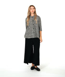 model in a wide leg pant with overlapping front panels, worn with a black and white button down blouse with 3/4 sleeves, a full body, and oversized contrast stripe pockets