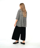model in a wide leg pant with overlapping front panels, worn with a black and white button down blouse with 3/4 sleeves, a full body, and oversized contrast stripe pockets