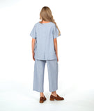 A woman modeling a light blue and white striped two-piece linen set consisting of a short-sleeve pullover top and matching cropped cargo pants, paired with brown loafers, against a plain white studio background.