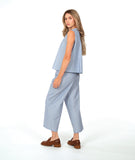 model in a sleeveless blouse with a soft blue and white stripe with a yellow textured dot pattern. worn with a wide leg matching pant and brown shoes