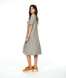 A woman modeling a loose, short-sleeve midi dress with a gray and white vertical stripe pattern with a textured yellow dot. dress has an asymmetrical body, scoop neck and elbow length sleeves