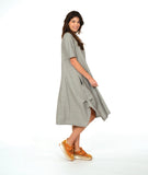 A woman modeling a loose, short-sleeve midi dress with a gray and white vertical stripe pattern with a textured yellow dot. dress has an asymmetrical body, scoop neck and elbow length sleeves