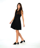 model in a sleeveless, knee length dress with an asymmetrical skirt. dress is black with a small textured dot print