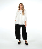 model in a white pullover top with a textured swirl print, round neck, and splits at the hips and front center. worn with a matching black pant with a slight barrel leg