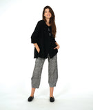 model in a black pullover top with a textured swirl print, round neck, and splits at the hips and front center. worn with a black and white striped pant with a slight barrel leg
