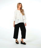 model in a wide leg black pant with a textured swirl pattern, worn with a matching white pullover with large godet inserts at the sides, detailed with buttons and open splits