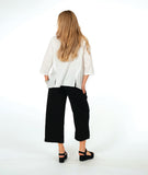 model in a wide leg black pant with a textured swirl pattern, worn with a matching white pullover with large godet inserts at the sides, detailed with buttons and open splits