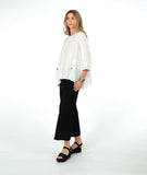 model in a wide leg black pant with a textured swirl pattern, worn with a matching white pullover with large godet inserts at the sides, detailed with buttons and open splits