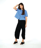 model in a short sleeve blue button down with a black wide leg barrel pant