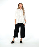 model in a white button down with a swirl texture. blouse has 3/4 sleeves and oversized rounded pockets at the hip. Worn with a wide leg black pant with the same texture