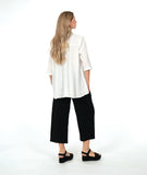 model in a white button down with a swirl texture. blouse has 3/4 sleeves and oversized rounded pockets at the hip. Worn with a wide leg black pant with the same texture
